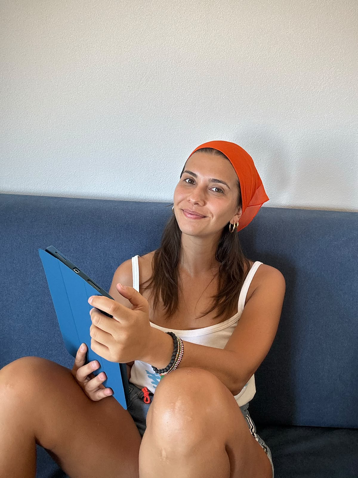 Marta sorridente sul divano con la bandana arancione e un tablet in mano